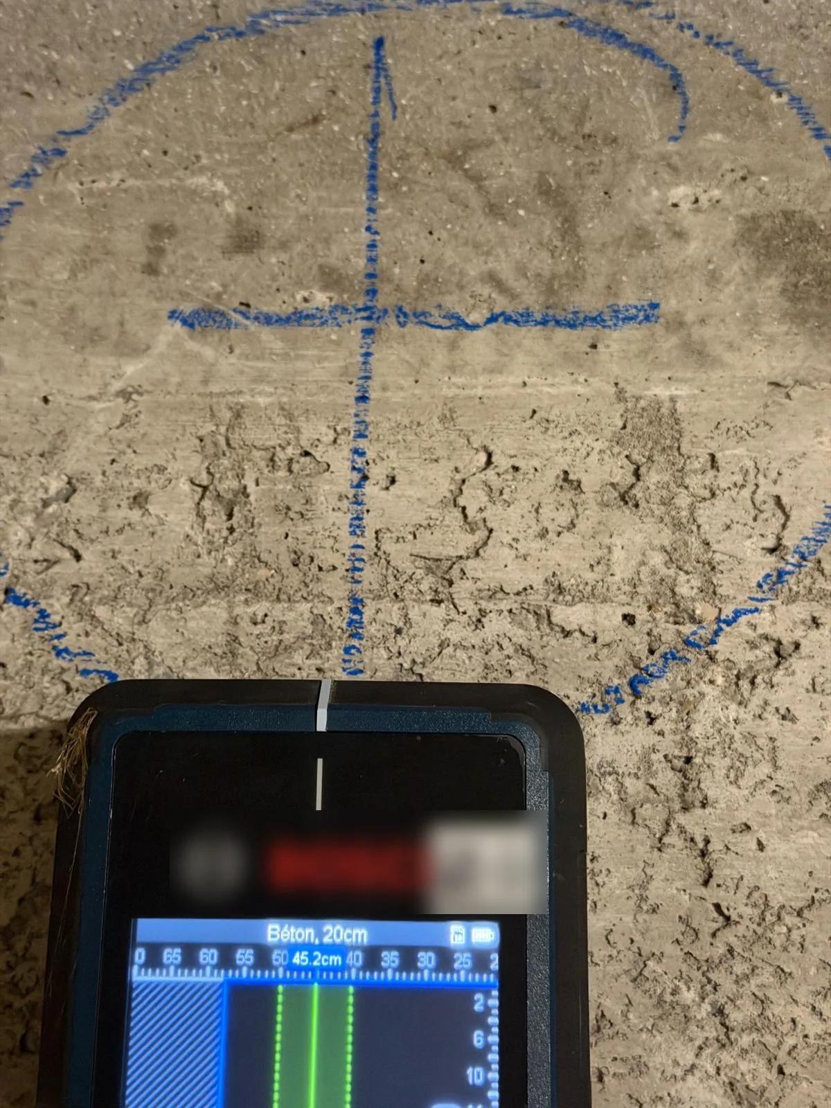 Détection d'armatures avant carottage : scanner de béton posé sous un emplacement marqué au crayon bleu sur un mur de sous-sol