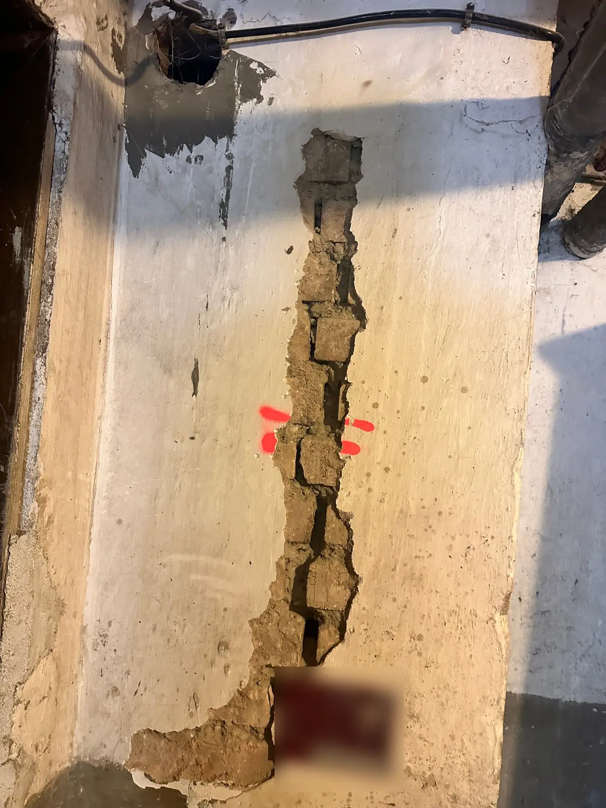 Fissure dégagée par sondage dans un mur de cave, repères de suivi à la bombe