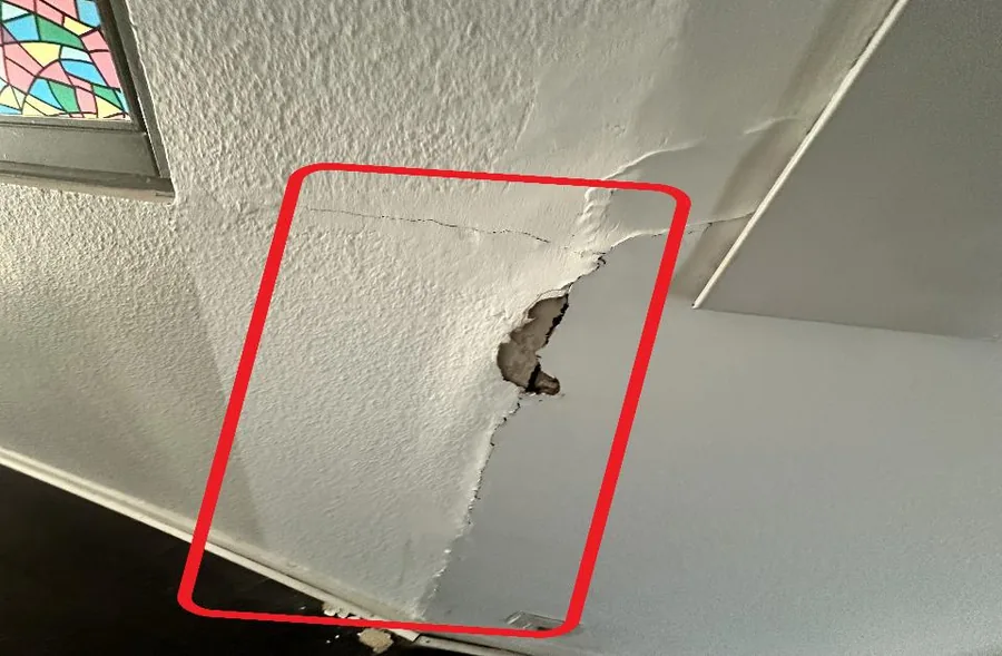 Fissure au plafond d'une cage d'escalier causée par la déformation d'un pan de bois