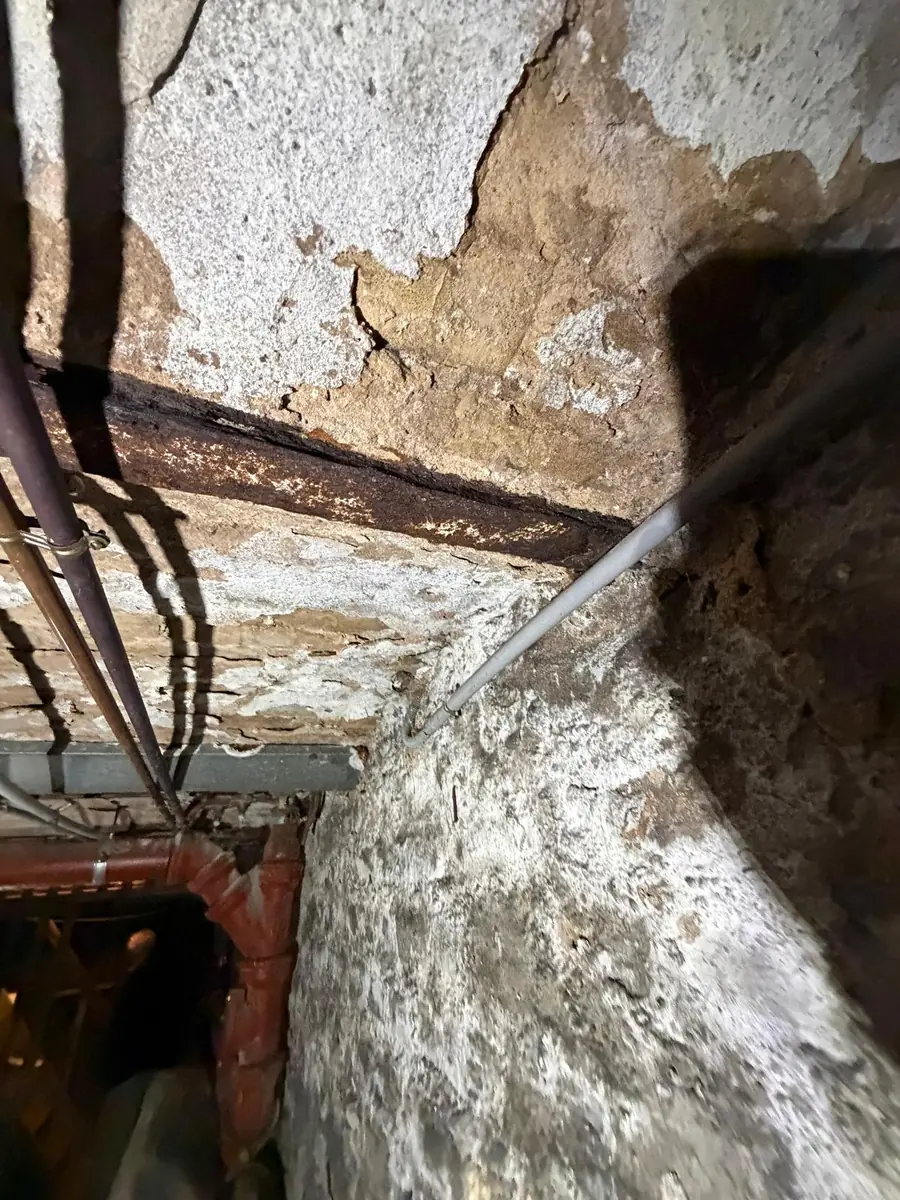 Poutre IPN avec rouille gonflante à son appui dans un mur de cave humide couvert de salpêtre