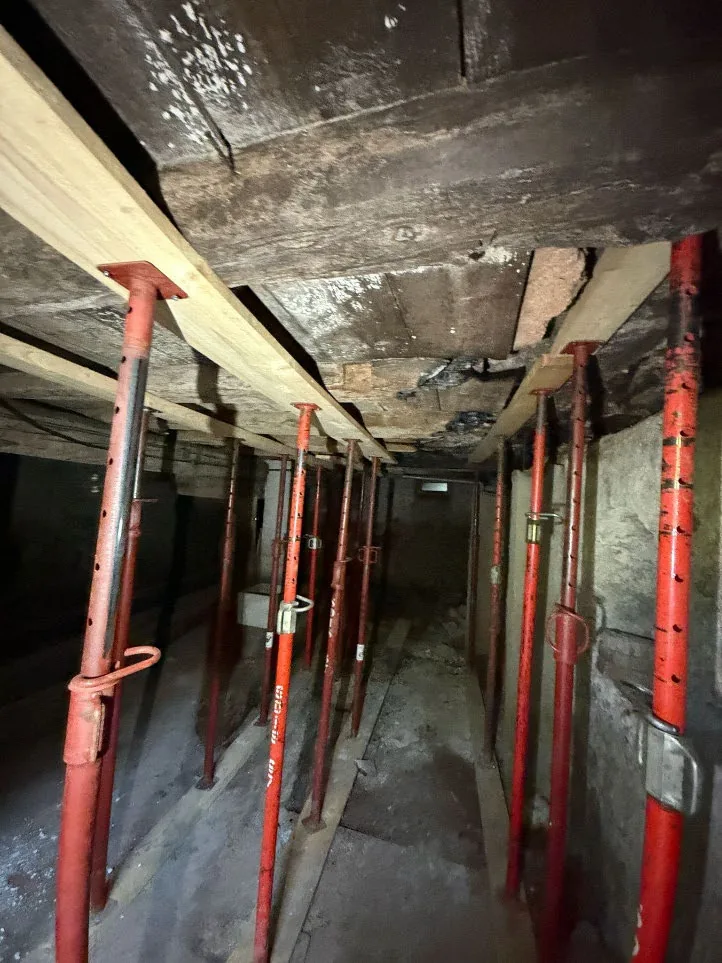 Plancher bois après incendie : solives brûlées étayées dans un sous-sol