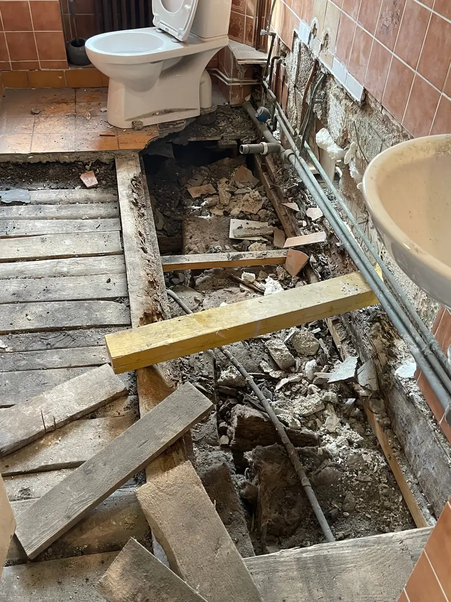 Plancher bois ouvert dans une salle de bain : poutre porteuse dégradée, planches et remplissage