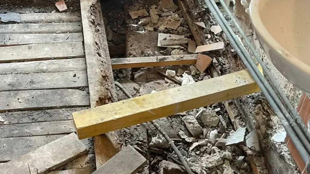 Poutre bois pourrie sous une salle de bain, plancher ouvert avec planches et remplissage