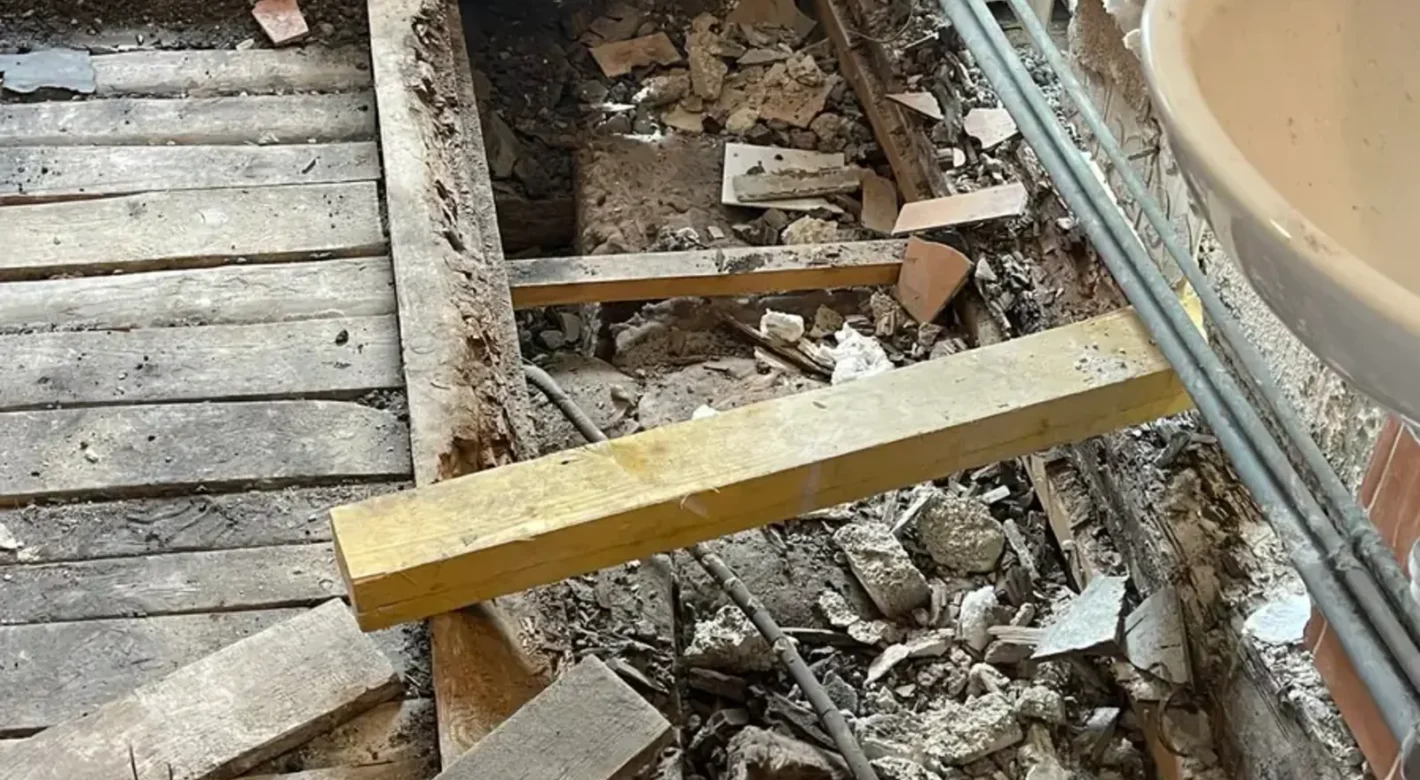 Poutre bois pourrie sous une salle de bain, plancher ouvert avec planches et remplissage